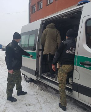 Fot. MOSG Zatrzymany cudzoziemiec wsiada do pojazdu służbowego w asyście funkcjonariuszy SG.