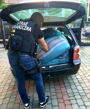 Fot. MOSG Funkcjonariusz SG przeszukuje samochód, w którym leżą worki z tytoniem.
