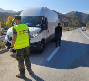 Funkcjonariusz SG podczas patrolu w Macedonii kontroluje pojazd. Funkcjonariusz SG podczas patrolu w Macedonii, w tle zatrzymani migranci.