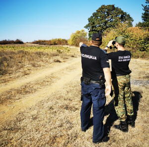 Funkcjonariusz SG i macdeoński policjant podczas patrolu. Funkcjonariusz SG podczas patrolu w Macedonii, w tle zatrzymani migranci.